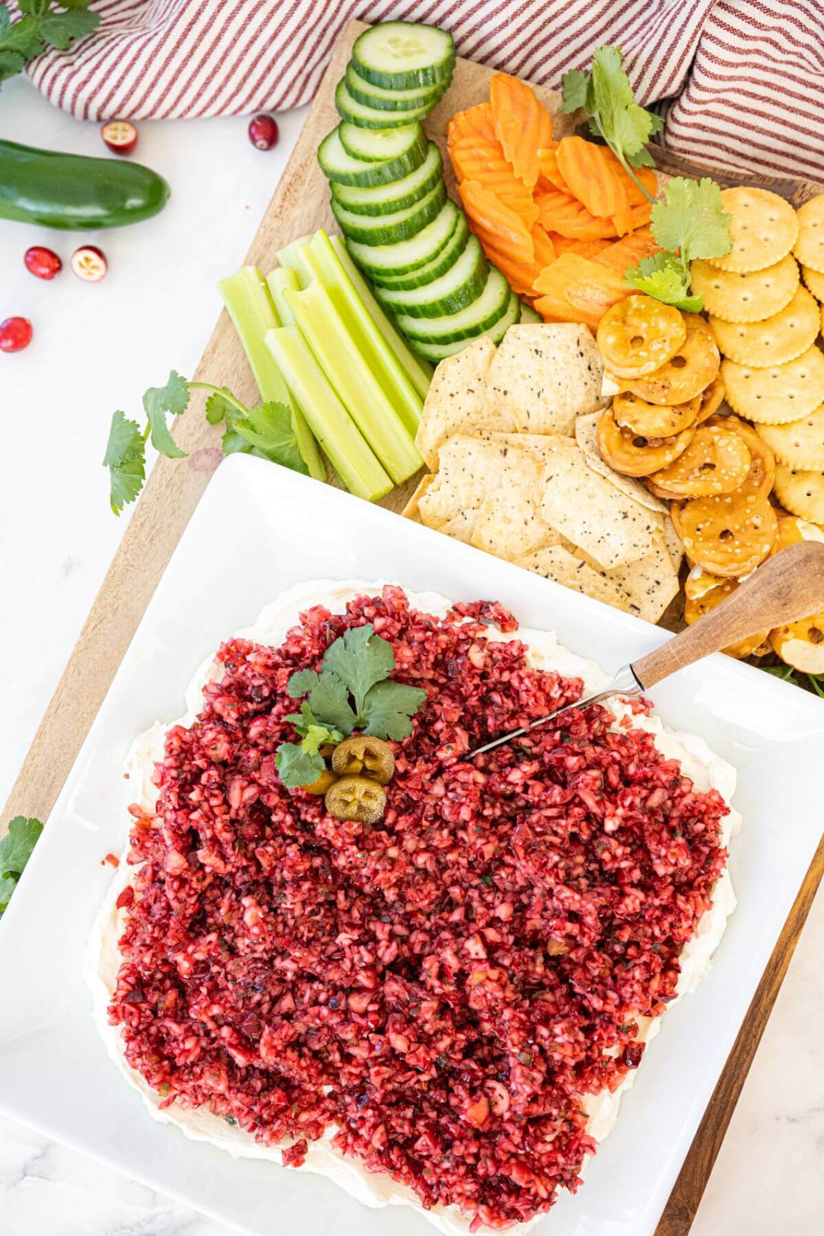 Square serving plate holds cranberry dip by vegetables and crackers.