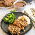 Cube Steak with mushrooms and onions is on a plate by gravy bowl.