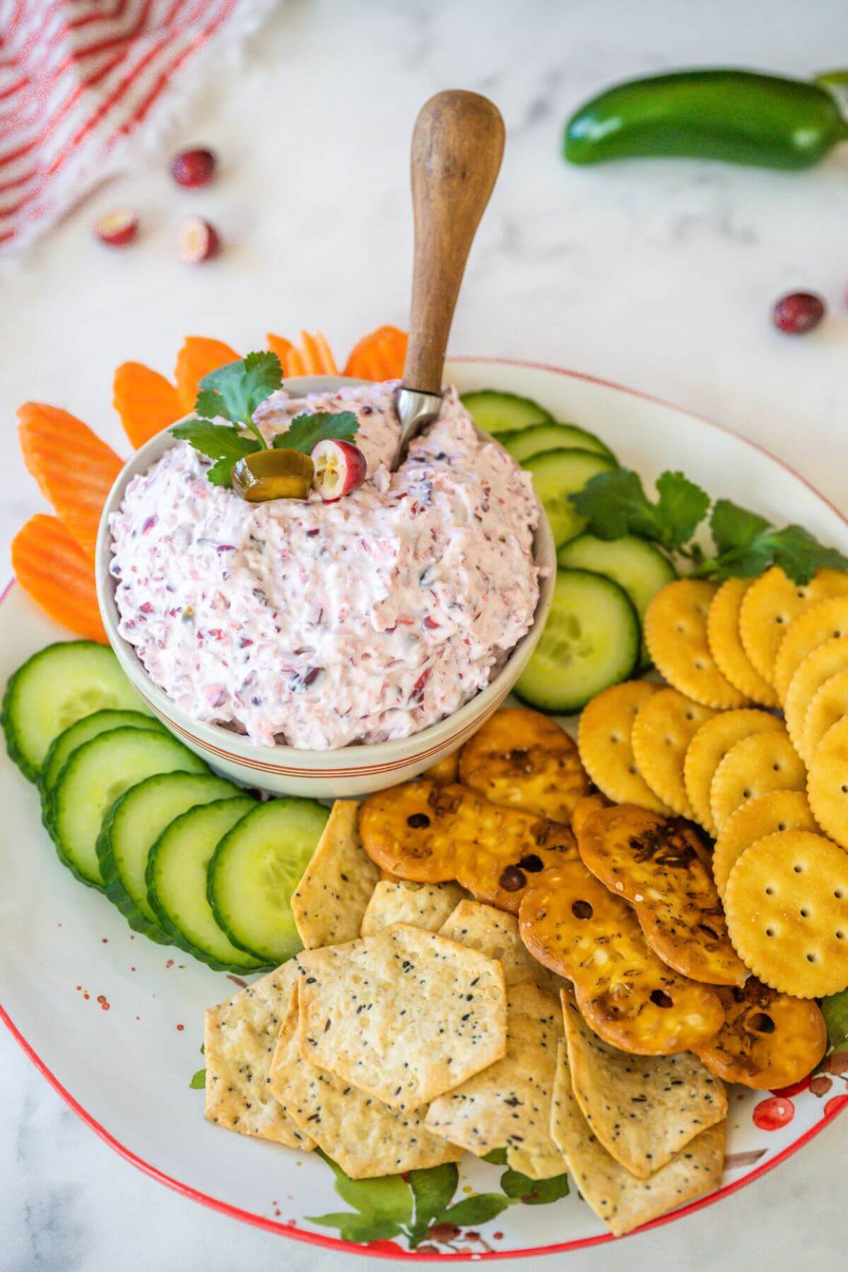 A bowl of dip is served on platter with crackers and veggies.