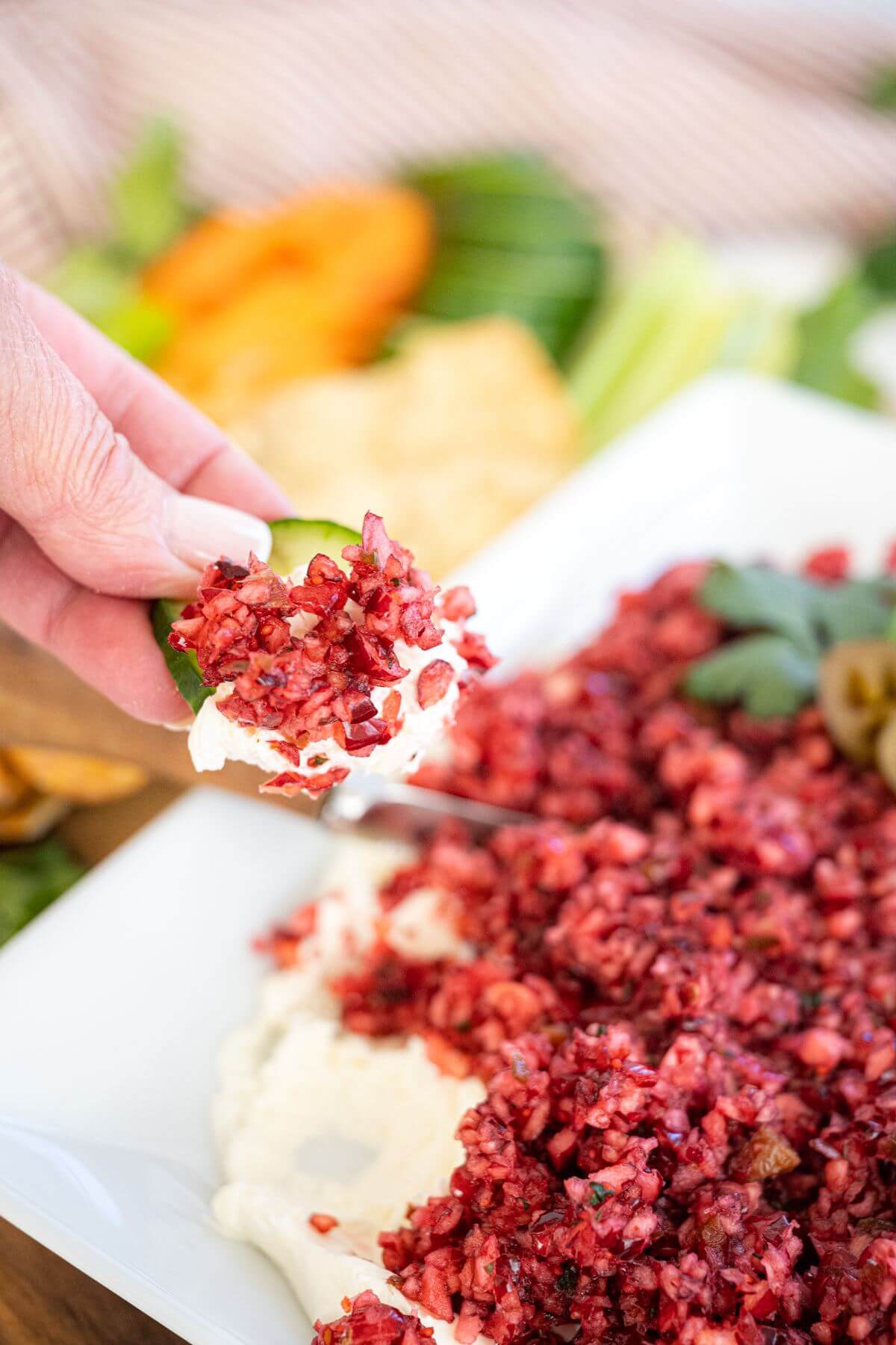 A hand dips a cucumber slice into the jalapeno cranberry dip.