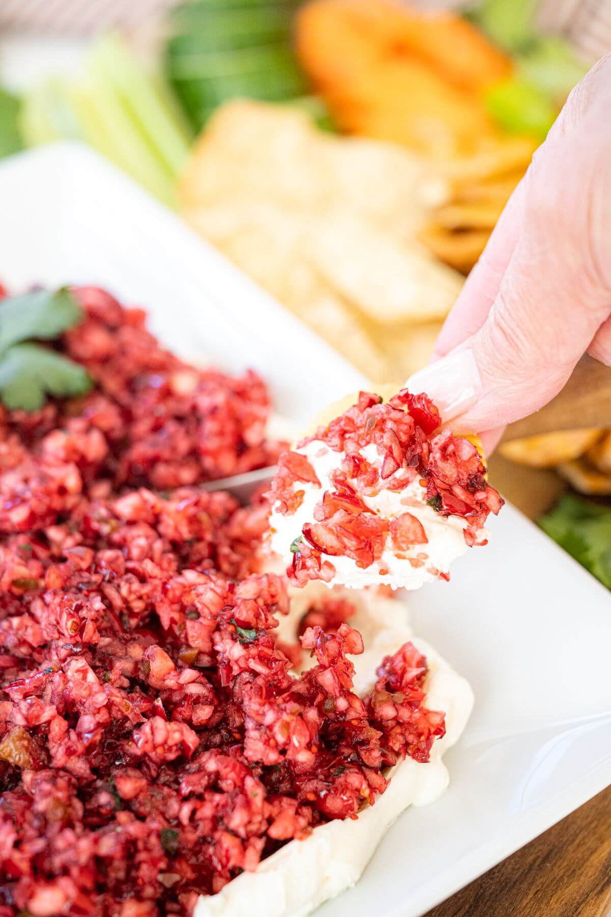 A hand is dipping food into the cranberry dip.