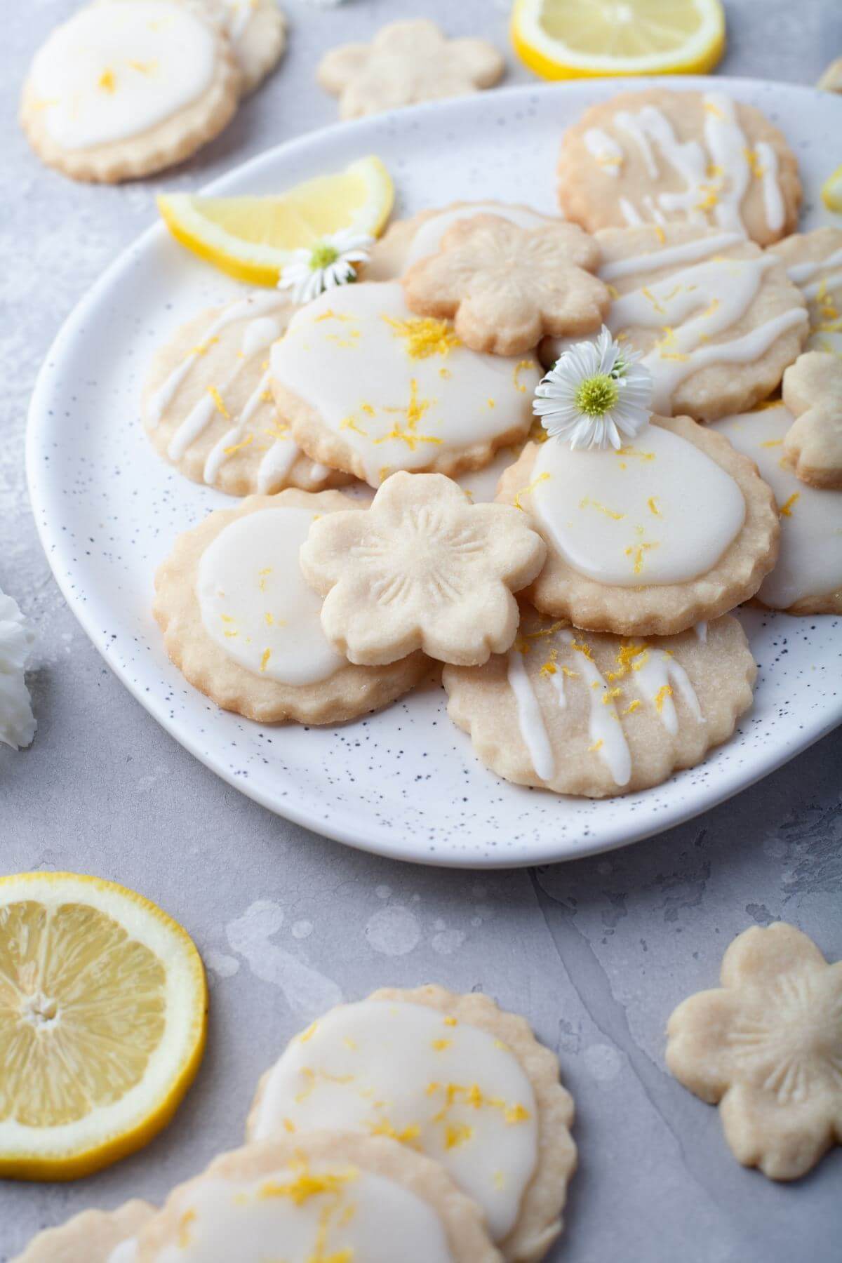 A platter of cookies is garnished with daisies and lemon slices.