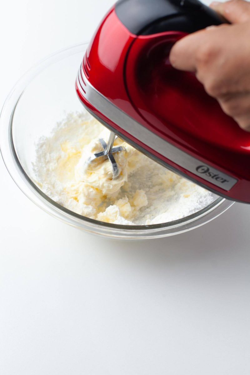 Someone is using a hand mixer to blend butter in bowl.
