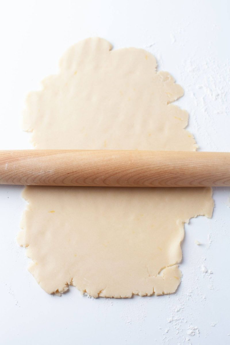 A wooden rolling pin rolls out sheet of dough.