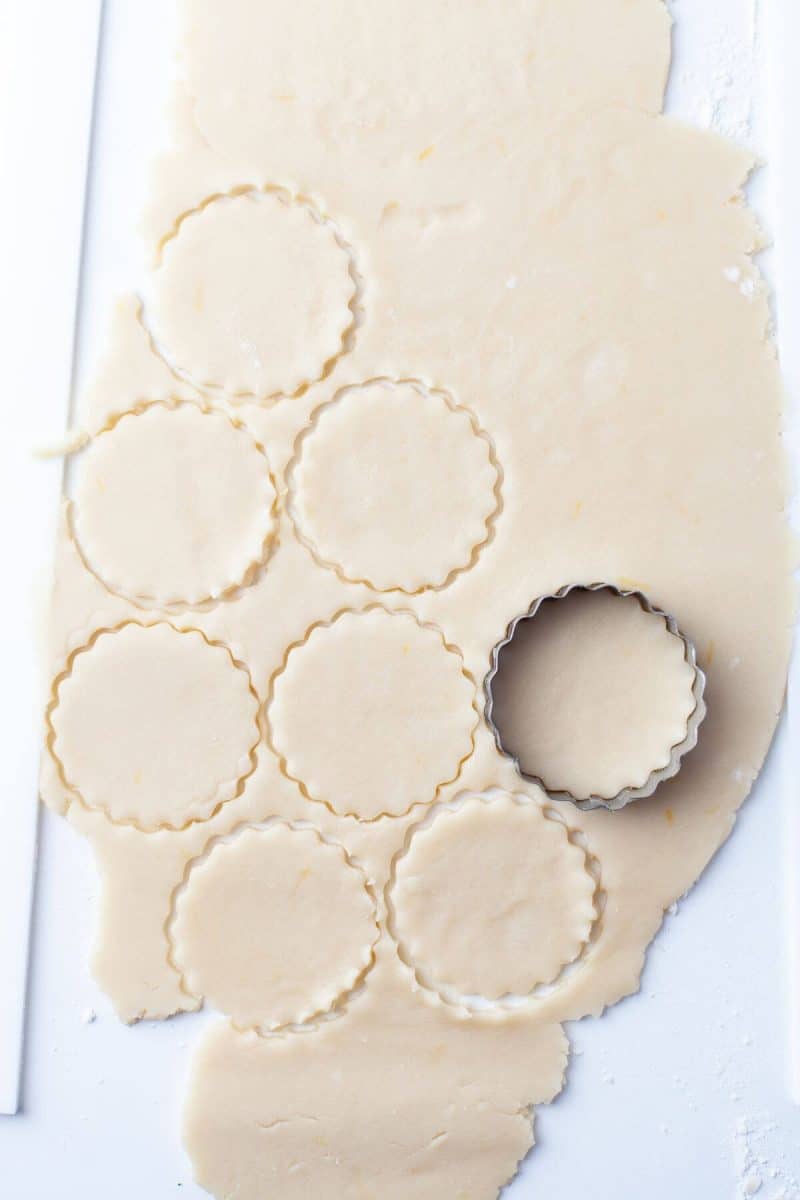 A cookie cutter is shown making imprints in rolled out dough.