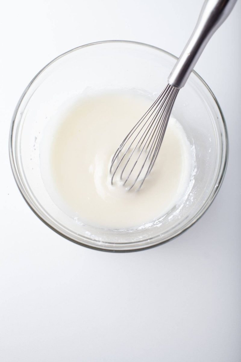 A whisk mixes icing ingredients in bowl.