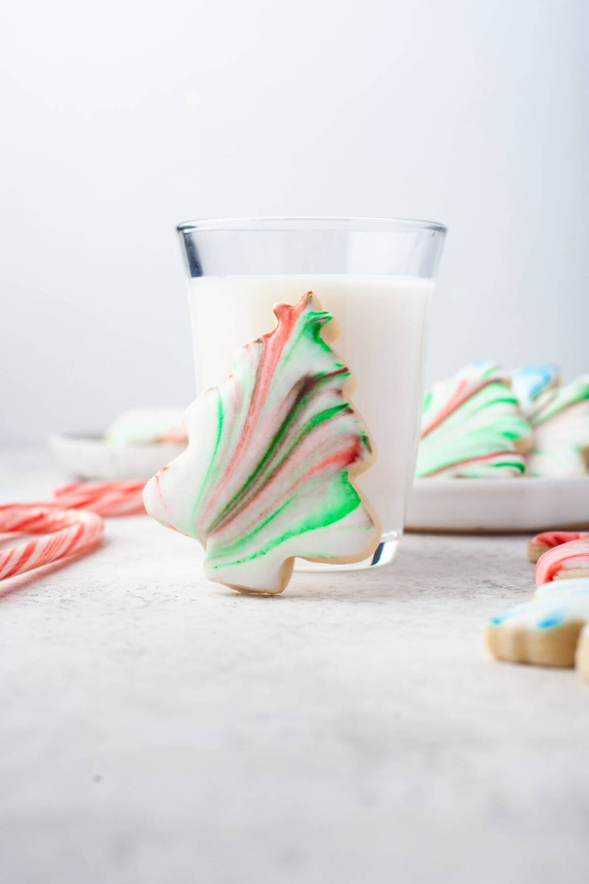 Marbled sugar cookie shaped like Christmas tree props up on milk glass.