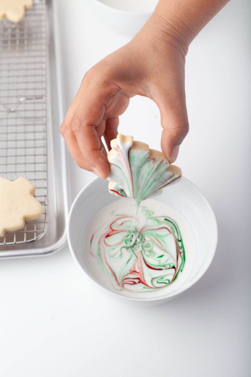 A hand dips cookie into marble icing.