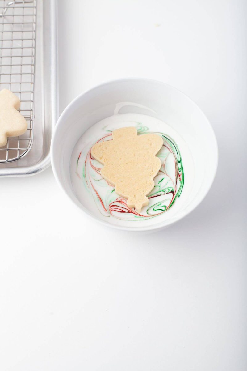 Christmas tree shaped cookie lies face down in bowl of royal icing.