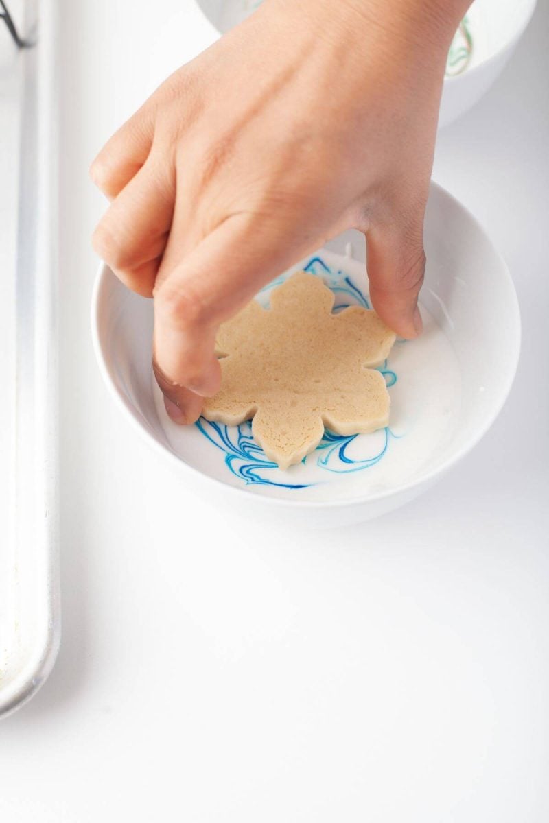 Someone places a leaf cookie face down in blue marble icing.