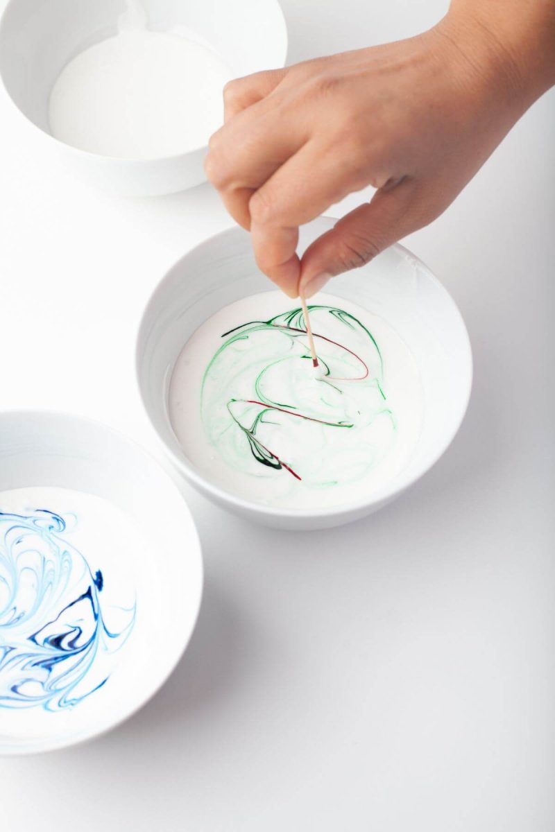 Someone holds a toothpick in icing bowl to swirl food coloring.