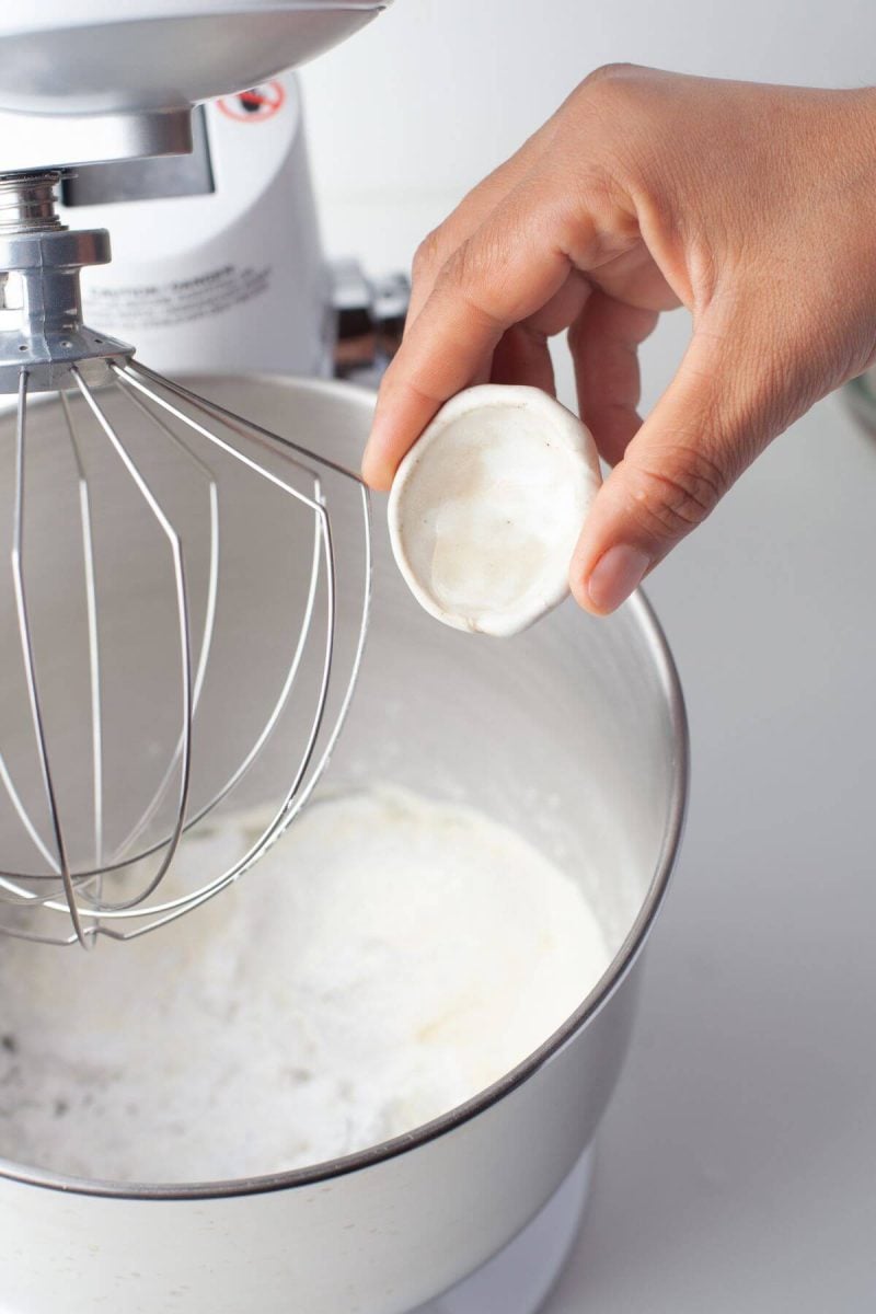 A hand pours baking powder into mixing bowl.