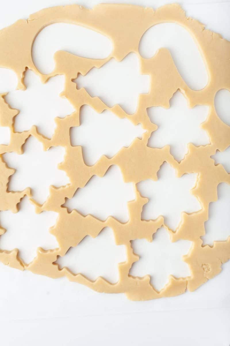 Cookie dough is cut out with cookie cutter shapes.