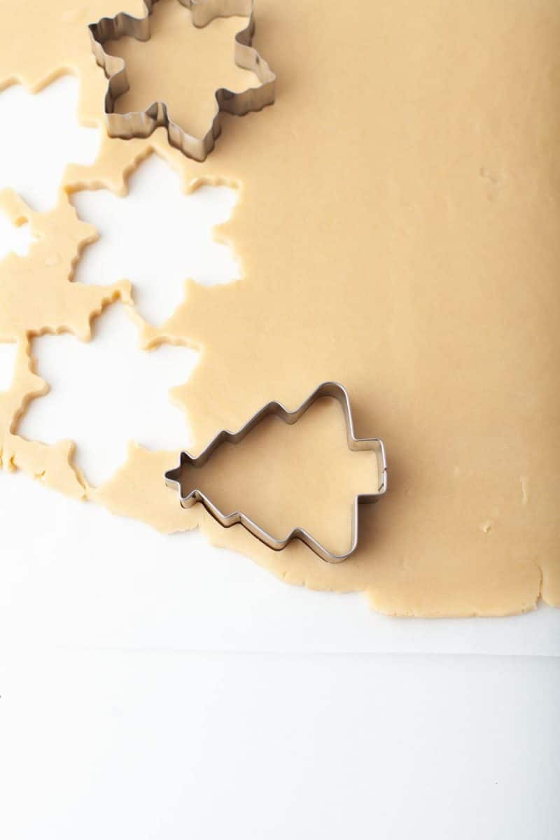 Rolled out cookie dough is cut with leaf and Christmas tree cookie cutters.