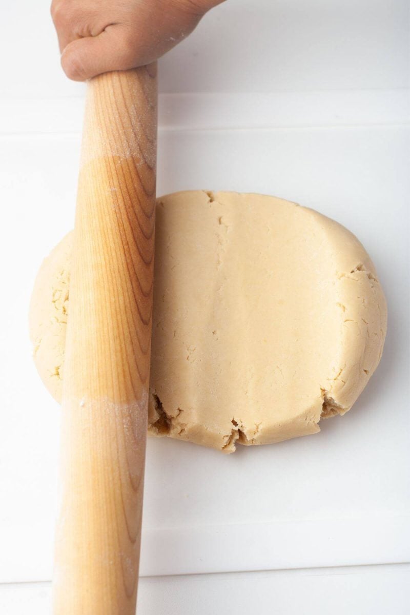 A hand rolls dough ball out with wooden roller.