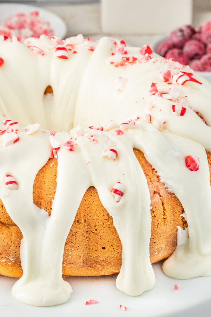 Peppermint Candy Cane Bundt Cake with Peppermint Cream Cheese Frosting with peppermints and berries behind.