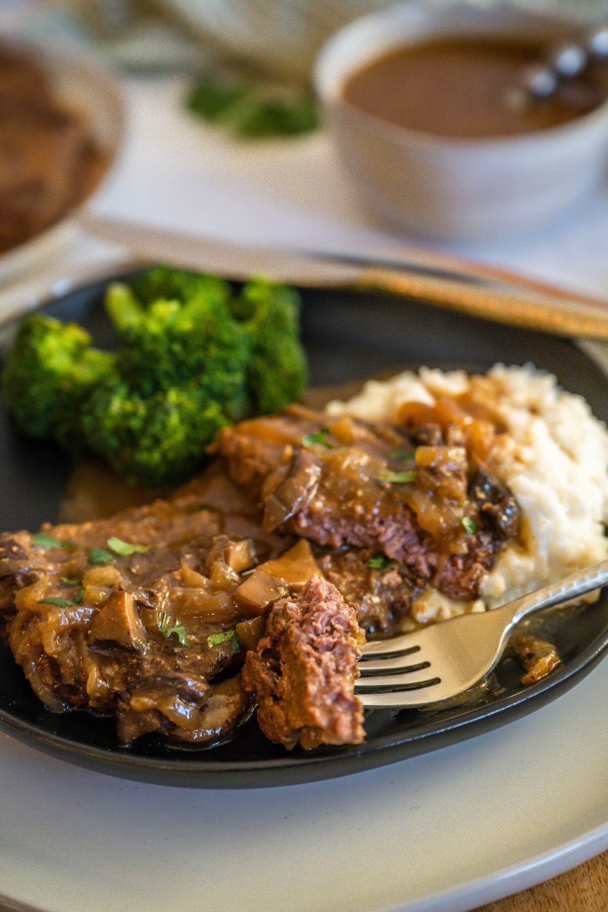 A piece of cube steak is on a fork laying on the plate of food.