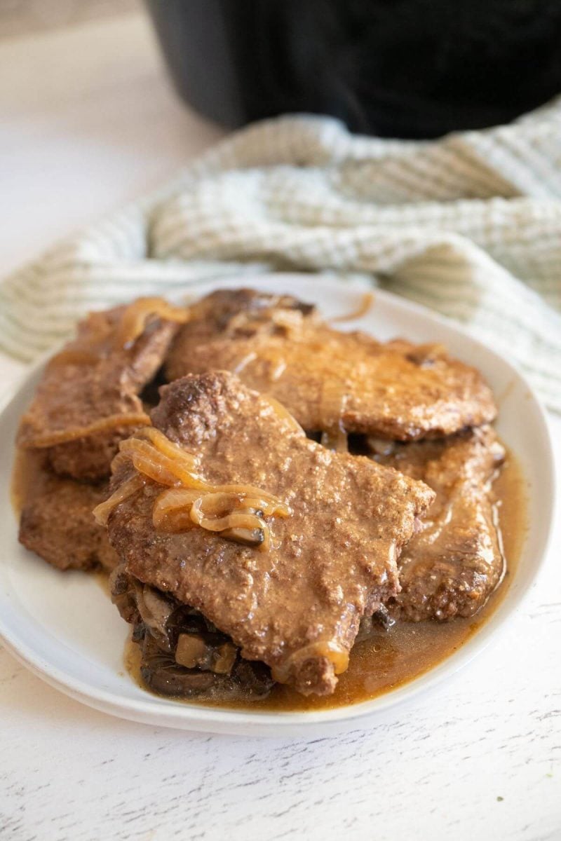 A plate of cube steak rests next to cloth and crockpot.