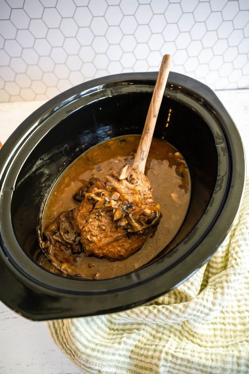 Cube steaks float in crockpot with wooden spoon.