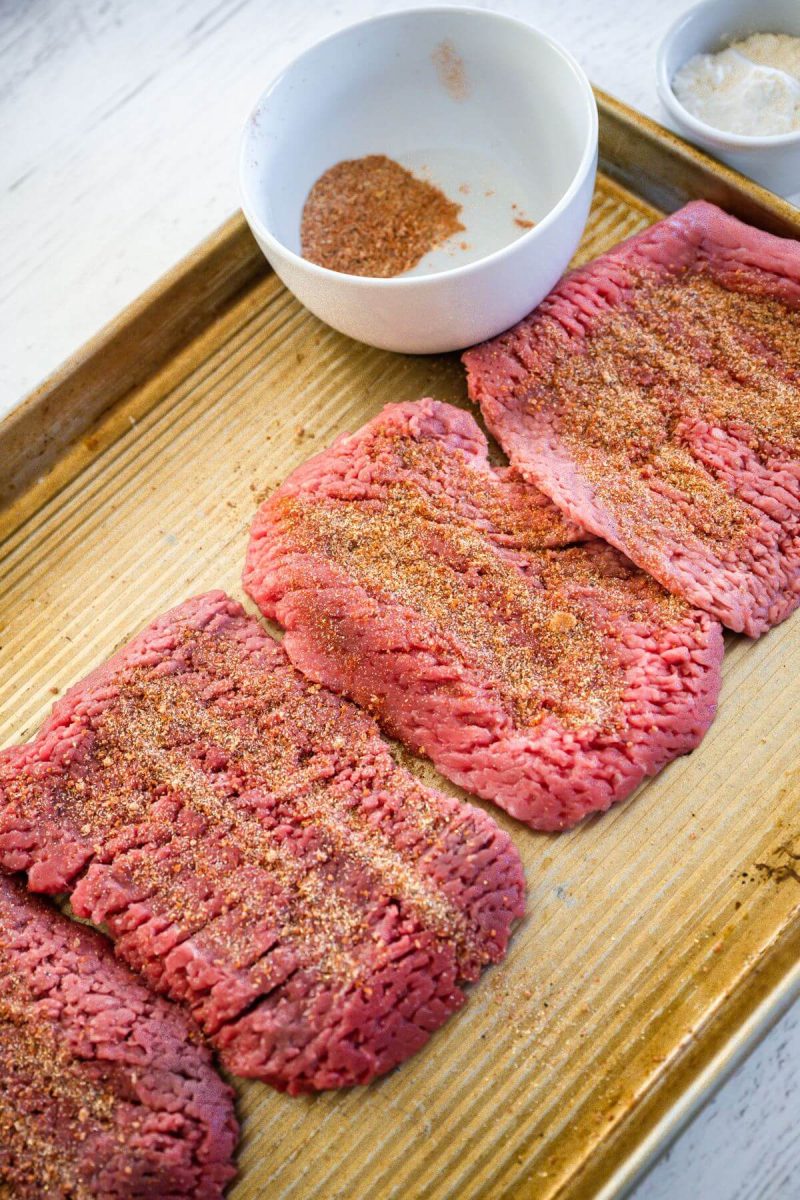 Raw cube steaks are sprinkled or rubbed with meat seasoning.