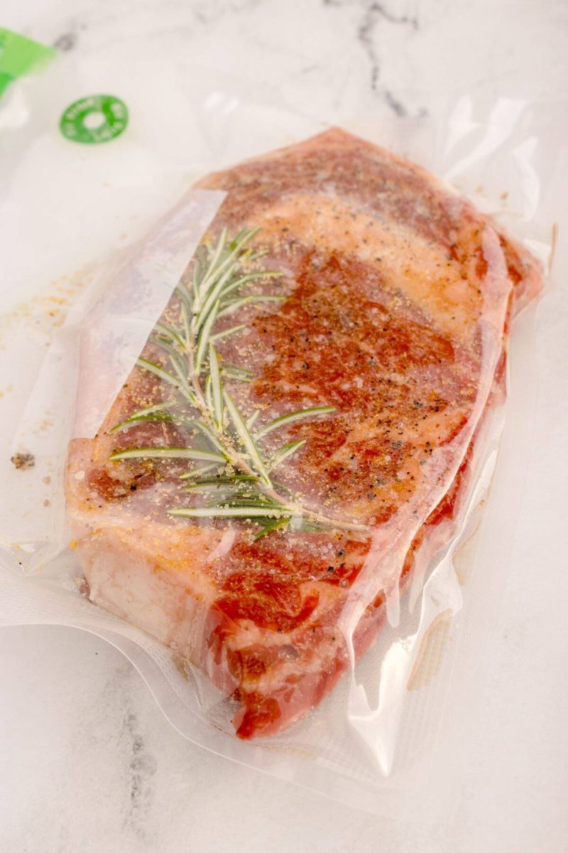 Steak and rosemary in a vacuum seal bag.
