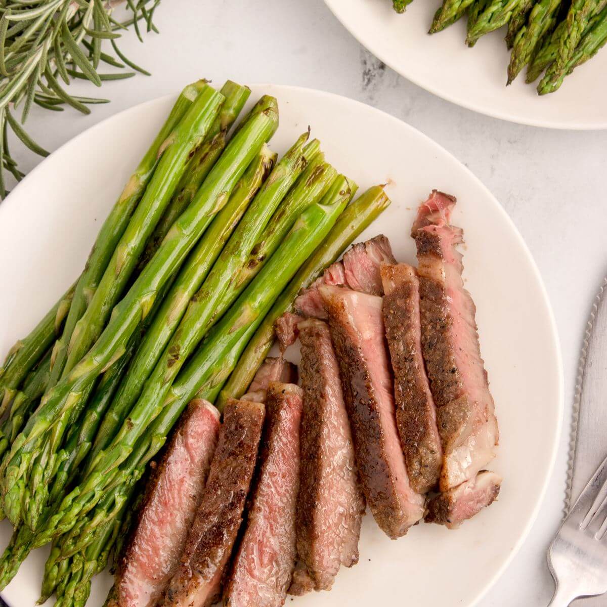 Slices of ribeye steak on plate with asparagus. 