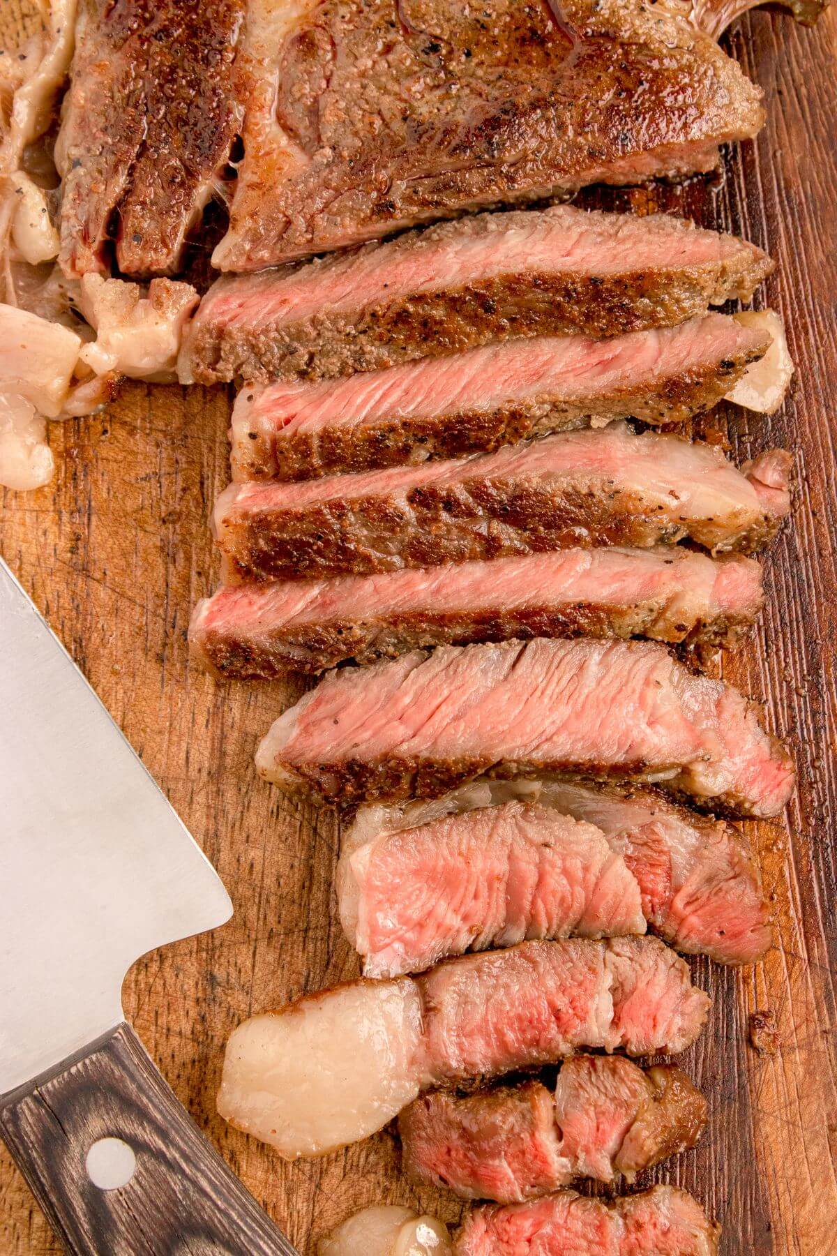 Ribeye slices by knife on cutting board.