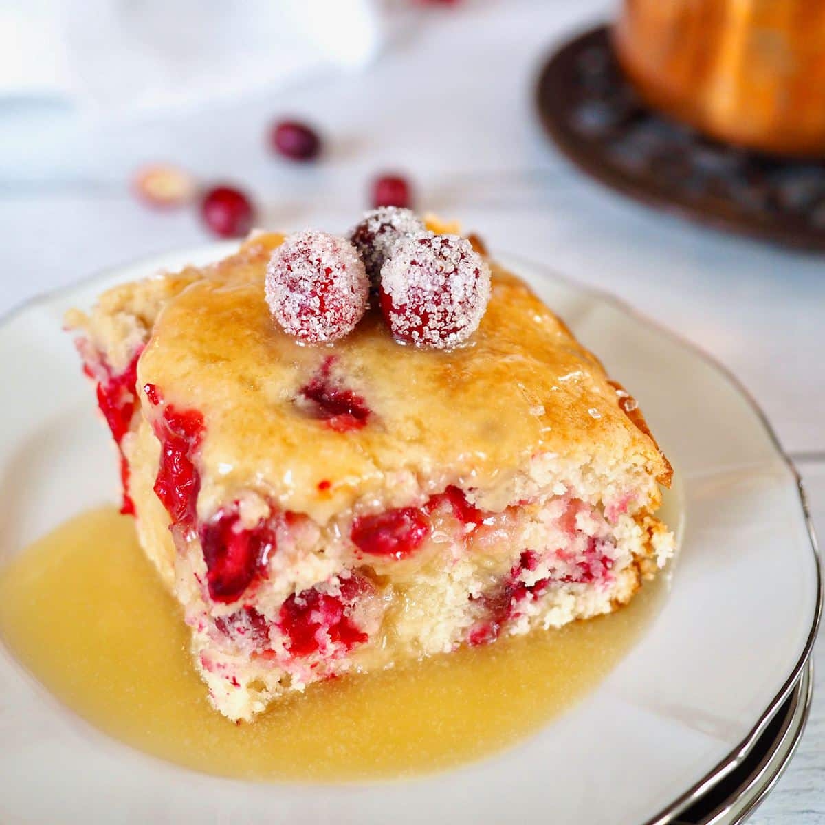 Slice of cranberry cake with butter sauce and topped with sugared cranberries.