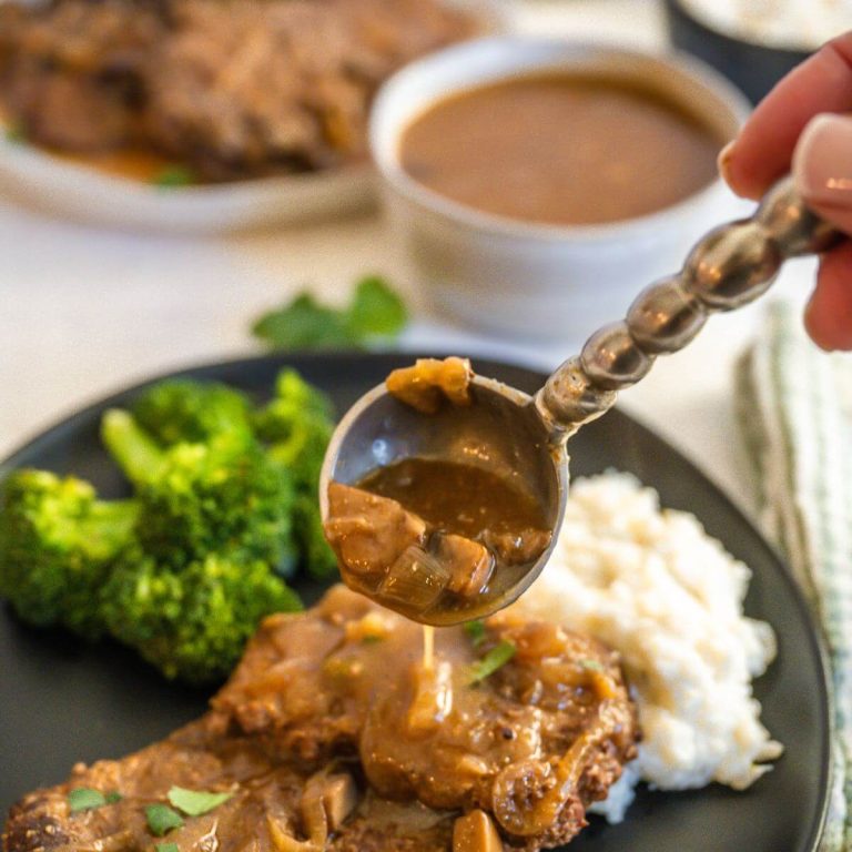 A hand pours spoon of gravy over cube steak on a plate.