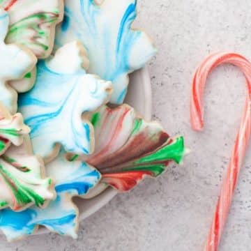 Bowl of colorful cookies are next to a candy cane.