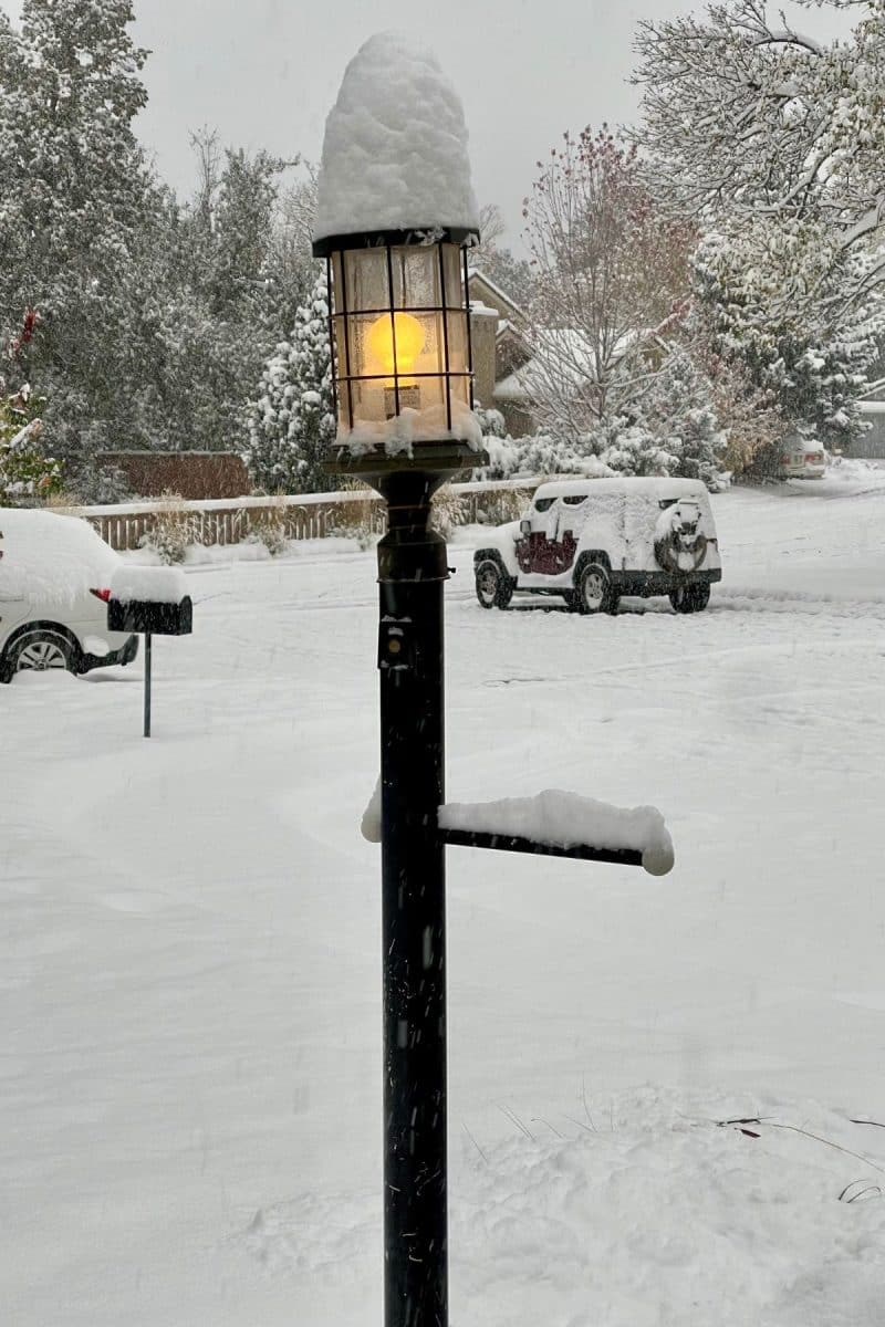 Lit lamppost topped with 6 inches of snow. 