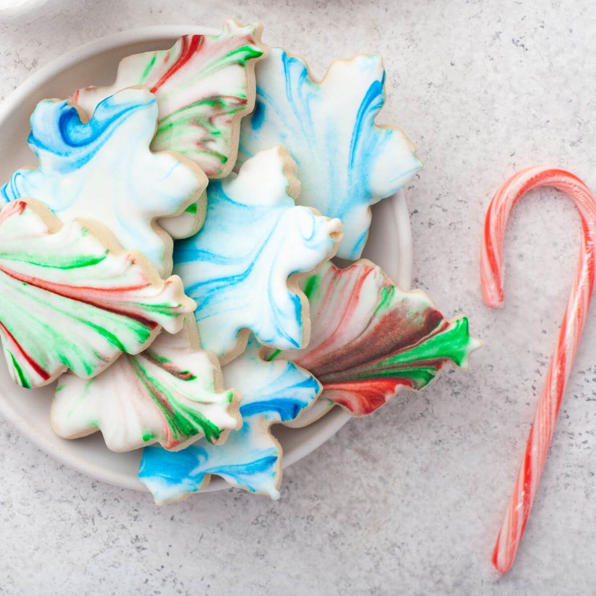 Bowl of colorful cookies are next to a candy cane.