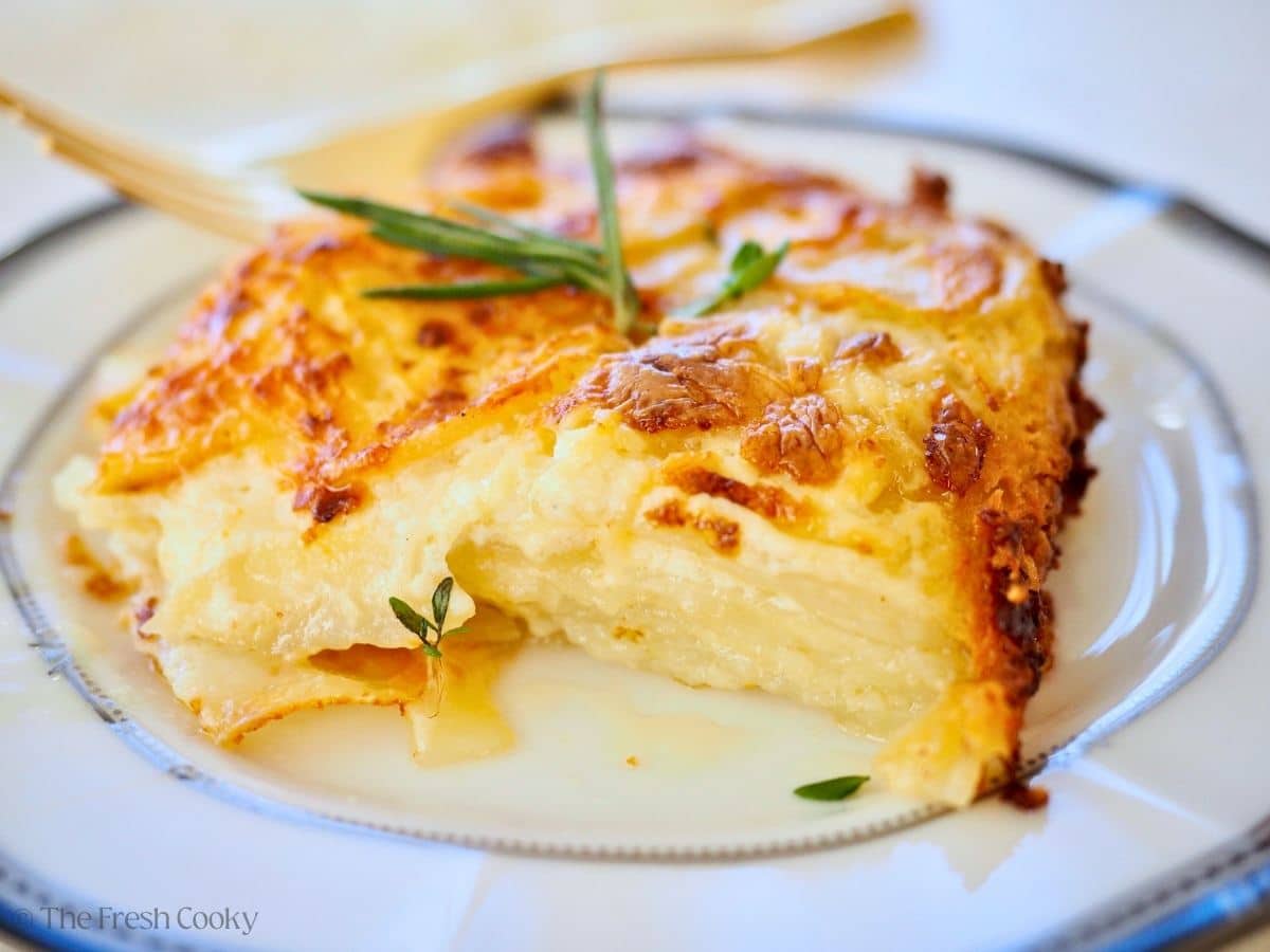 A cheesy slice of potatoes au gratin on a china plate with a gold fork.