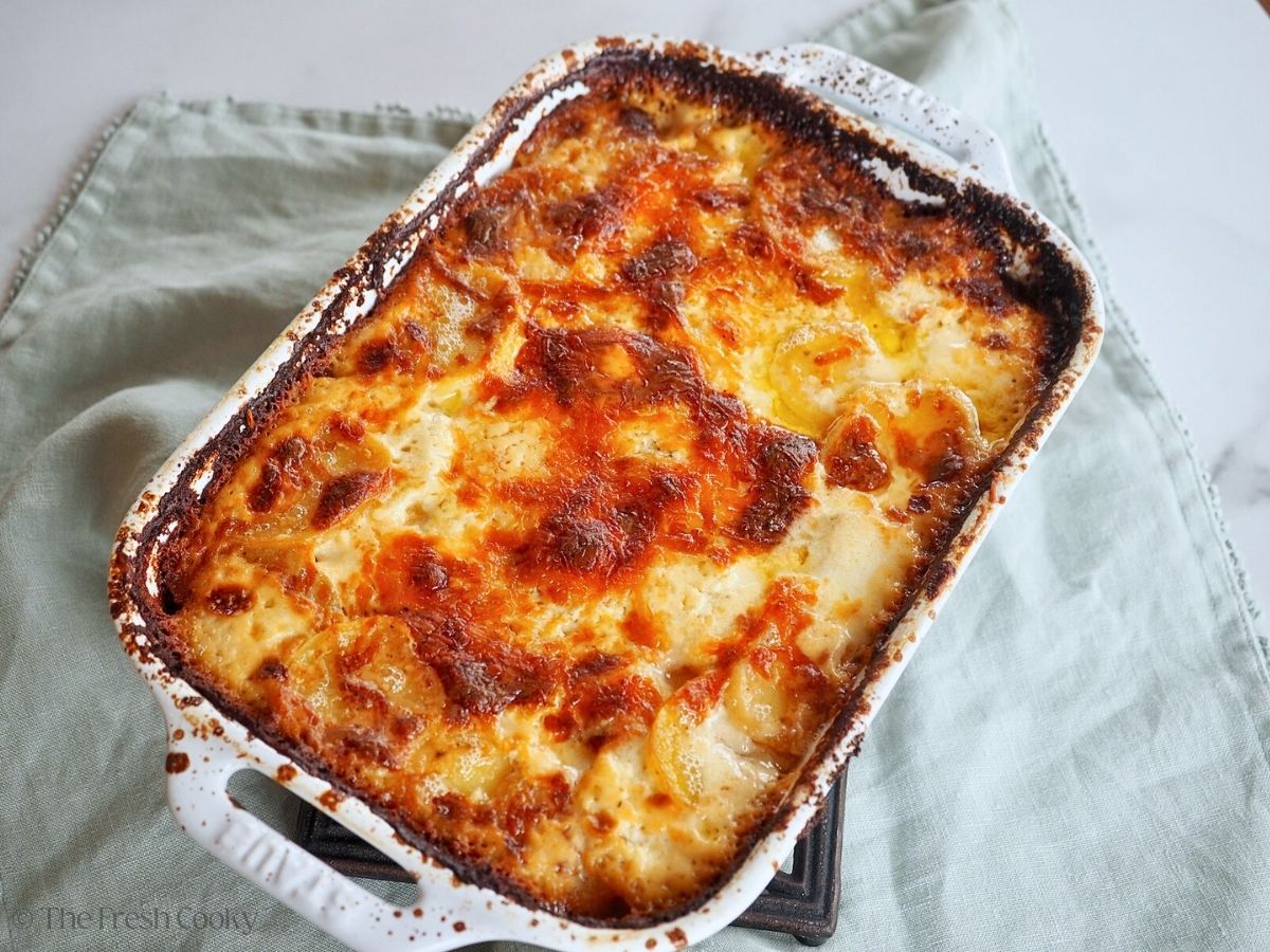 Golden potatoes au gratin in a white Staub baking dish.