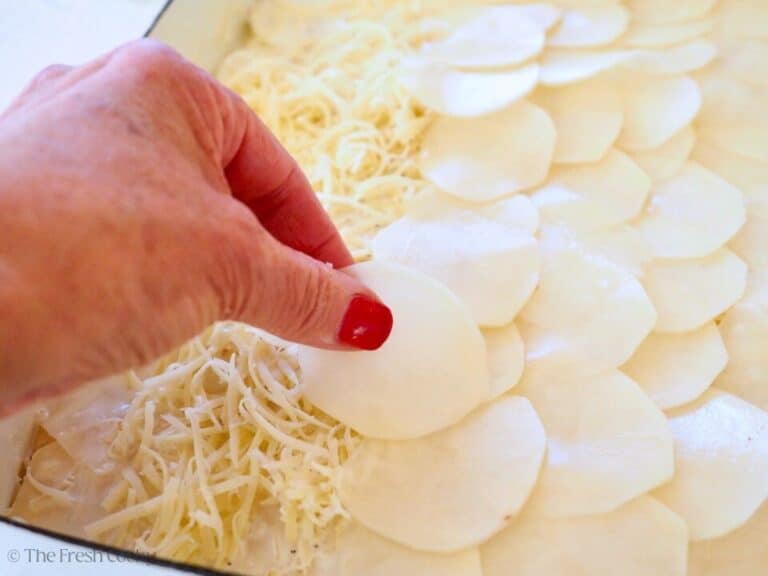 Hand placing thin slices of potatoes on top of shredded cheese.