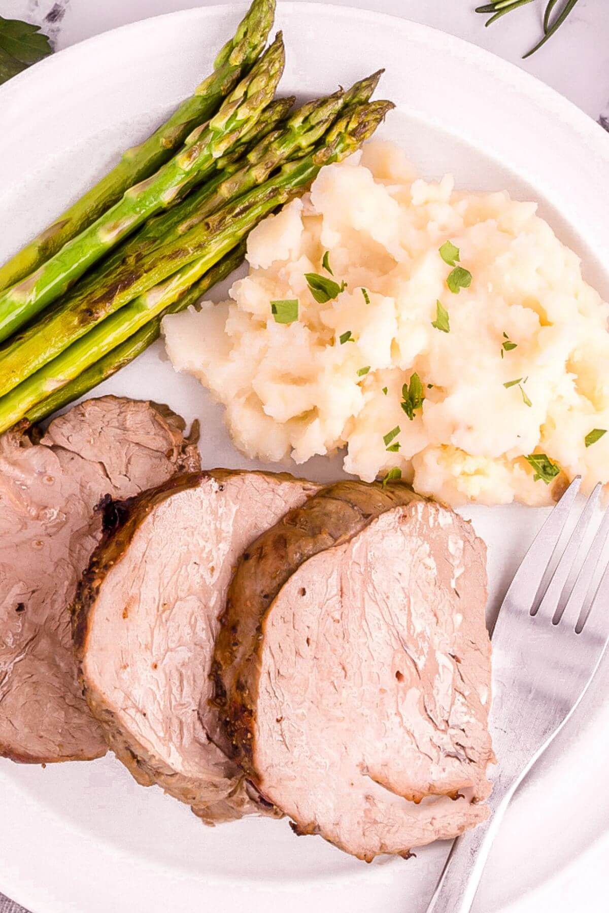 Slices of juicy tenderloin are shown next to mashed potatoes and asparagus.