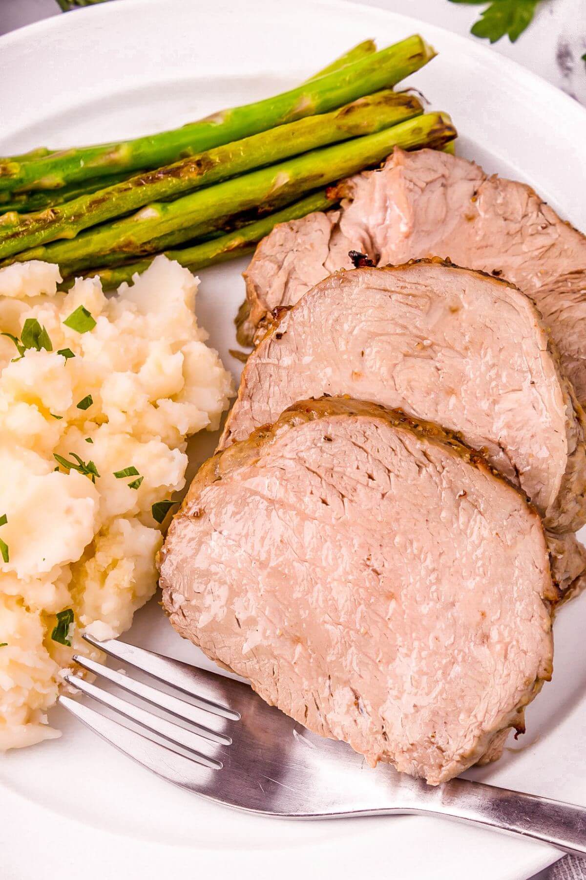 A plate is filled with tenderloin and veggies with a fork.