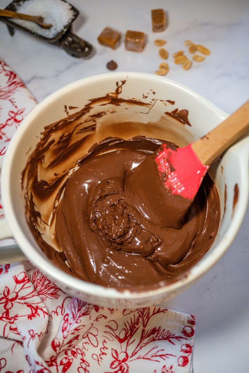 A spatula stirs melted chocolate in a mixing bowl.