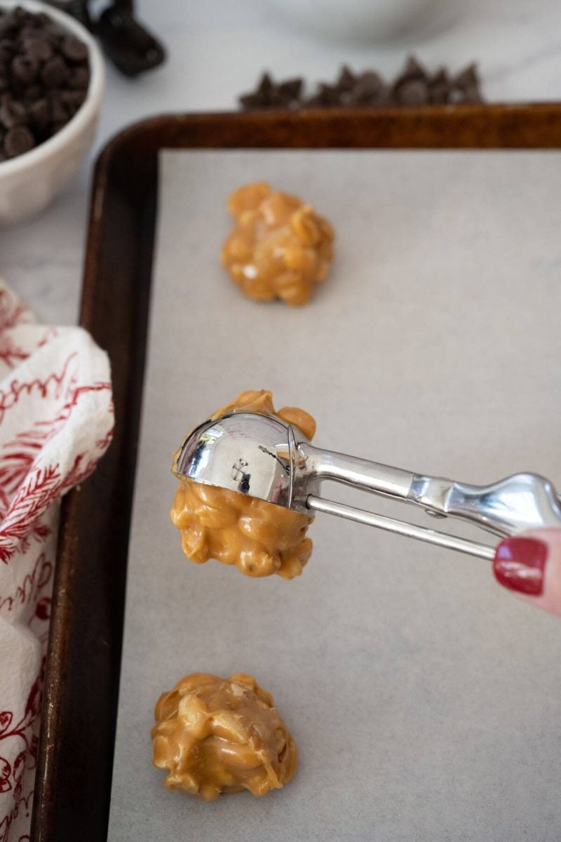 A cookie scoop drops a small amount of peanut cluster on a pan.