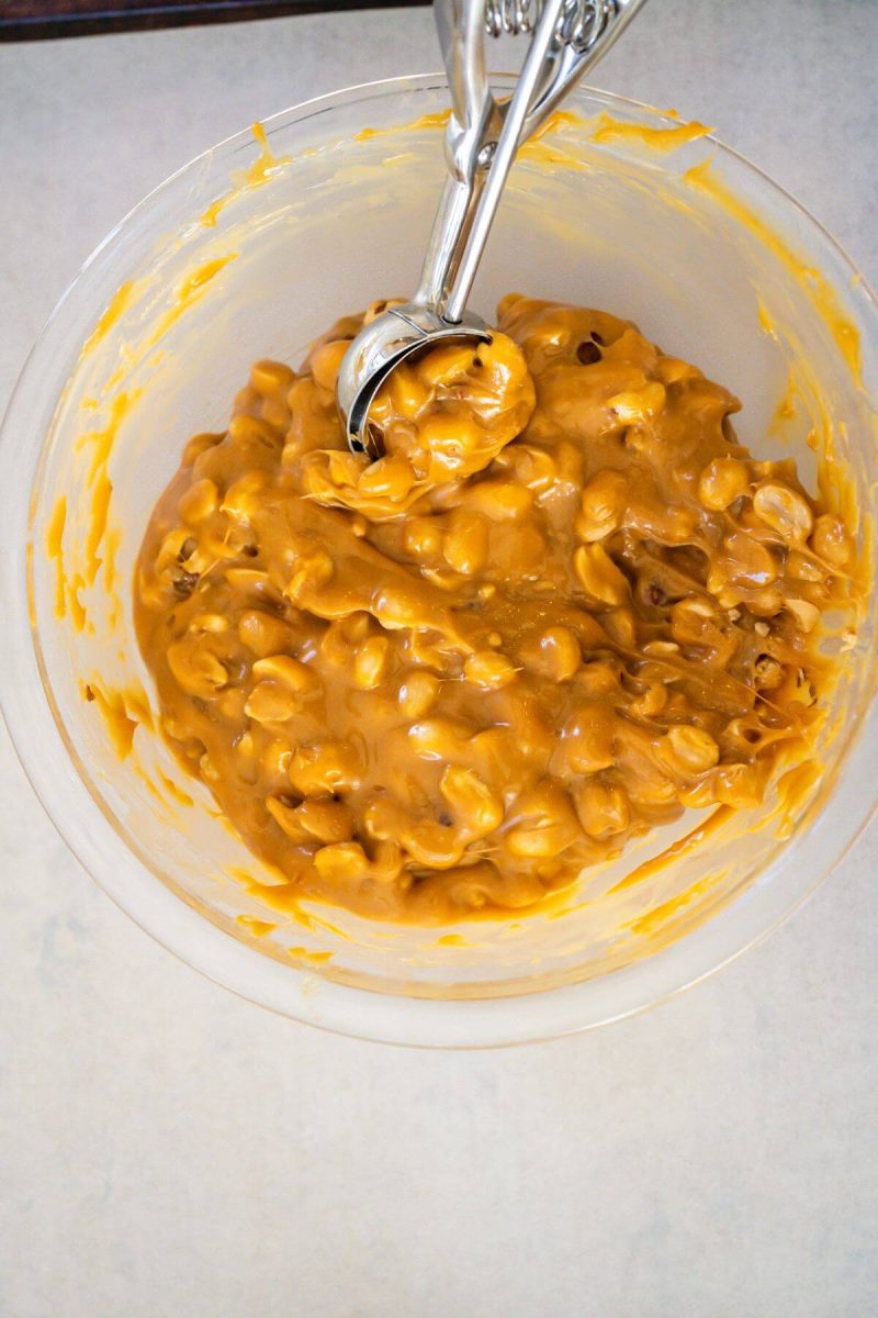 A cookie scoop reaches into the peanut caramel mixture in bowl.