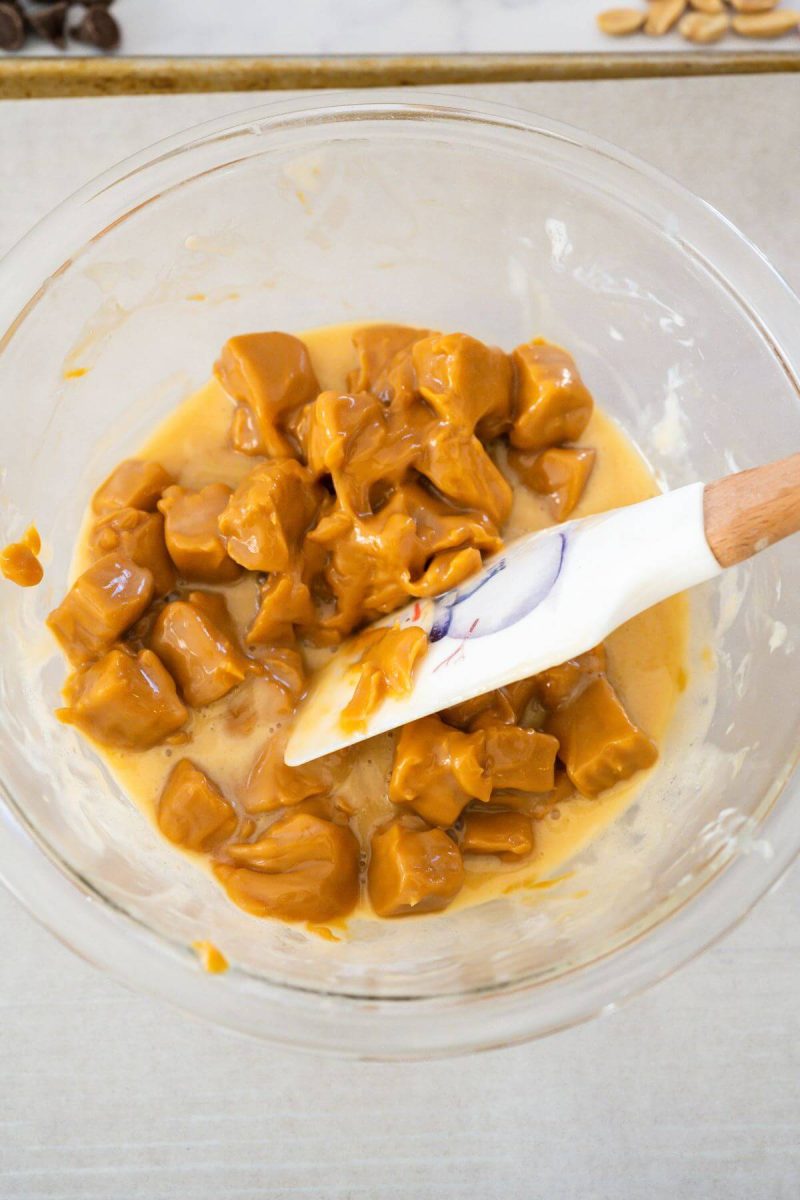 A spatula mixes caramels into liquid in a mixing bowl.