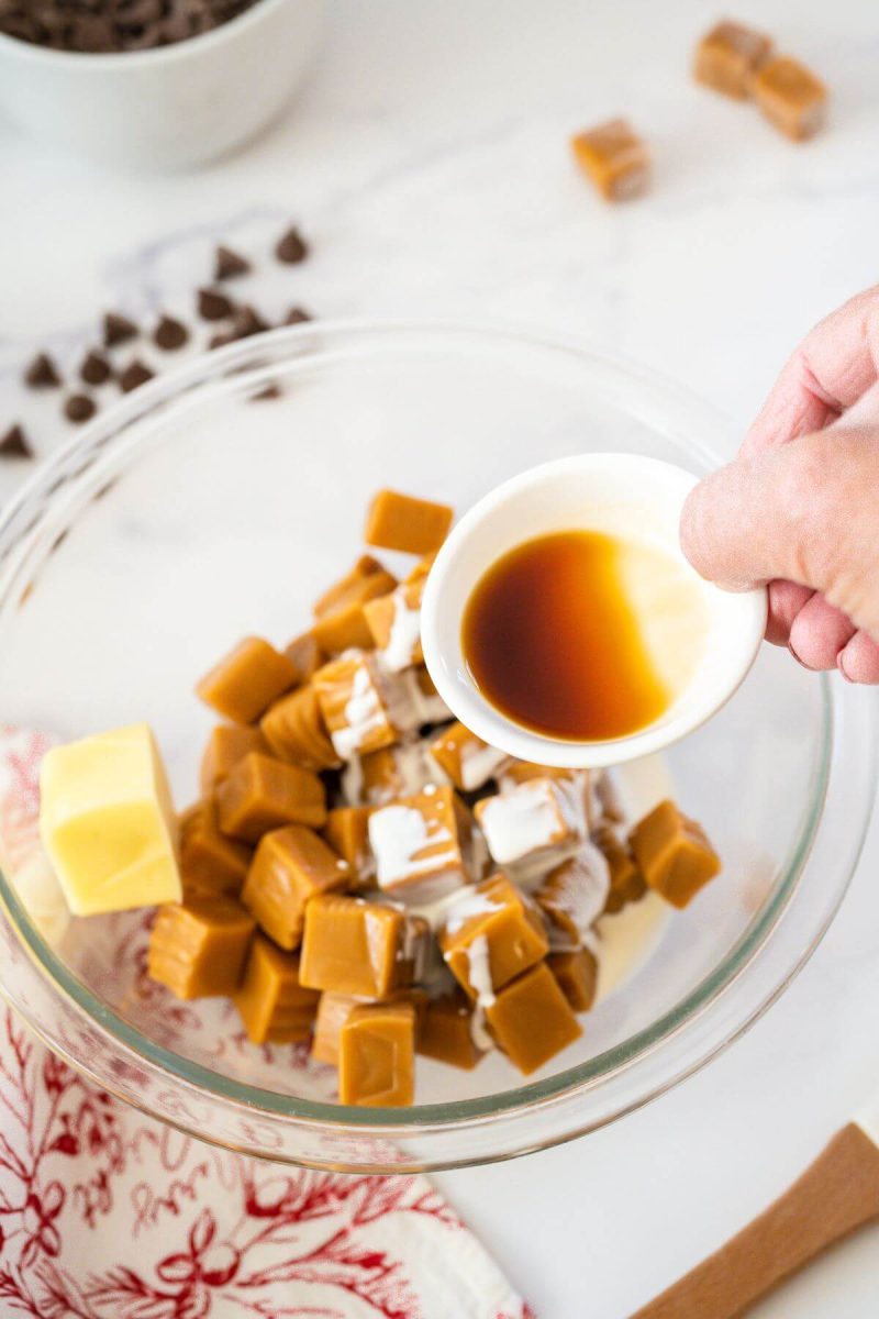 A hand pours a tiny bowl of vanilla into the bowl with caramels, and butter.