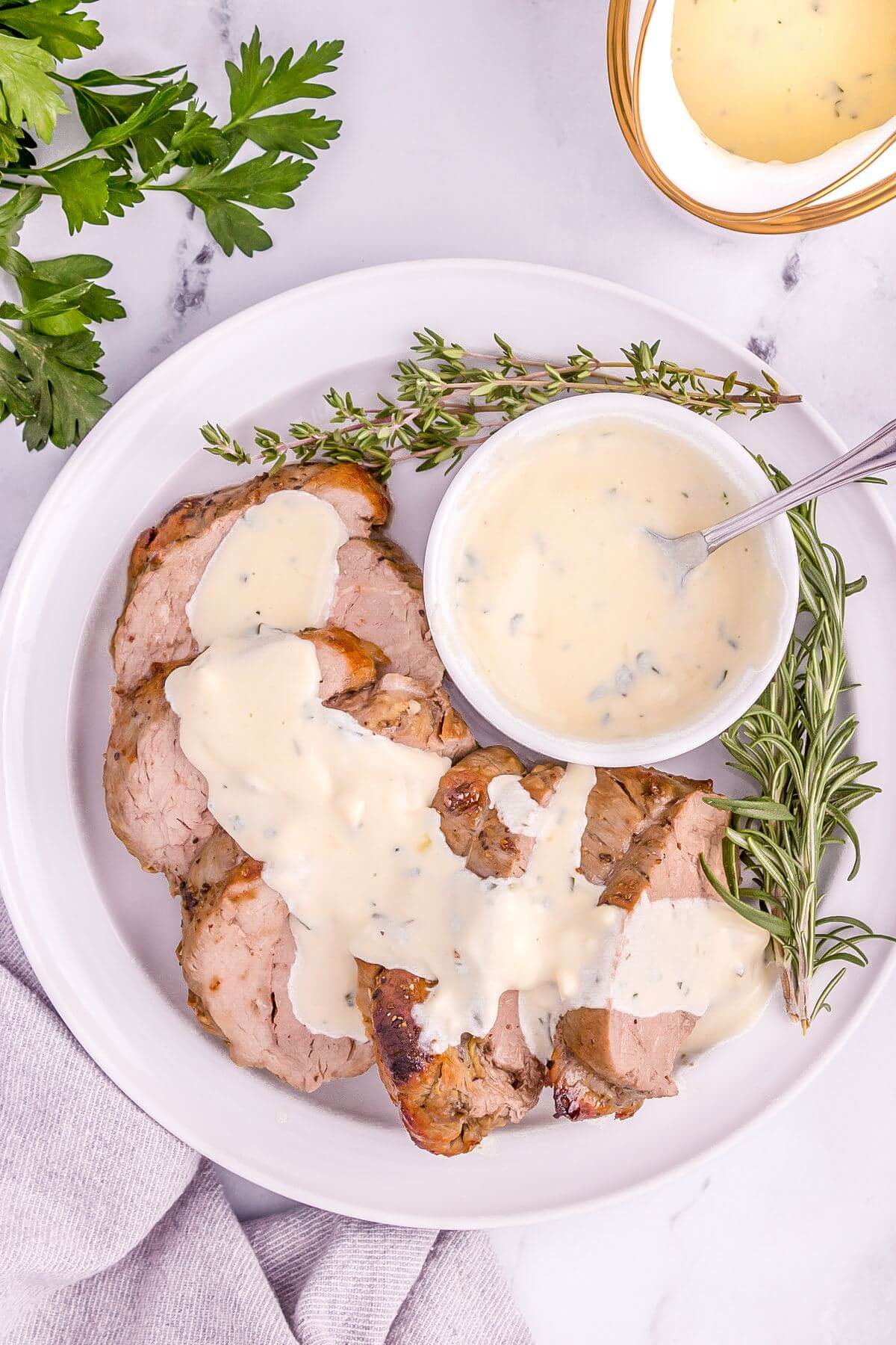 A filled plate includes small bowl of sauce, herb sprigs, and sauce covered meat slices.