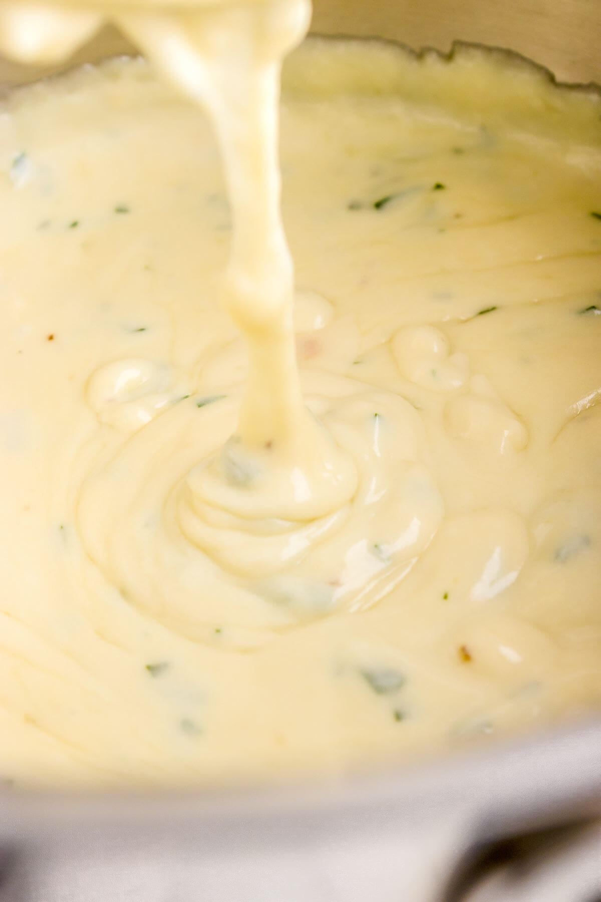 White sauce drips down into the whole pan of sauce.
