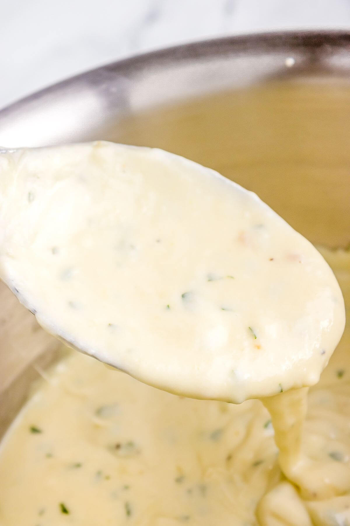 A spoon dips out thick creamy sauce from pan.