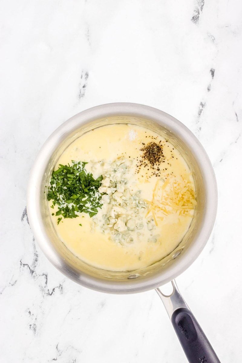 Cheeses, pepper, and parsley are sitting on top of sauce in saucepan.