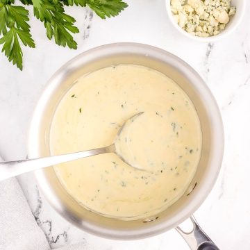 Creamy white sauce is in a bowl with a spoon resting in it.