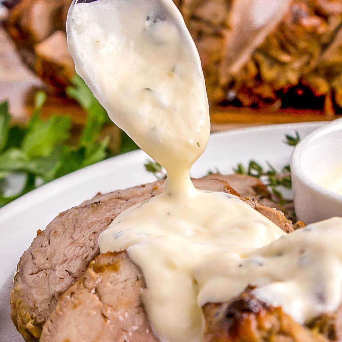 White sauce drips off of spoon from above onto meat on plate.