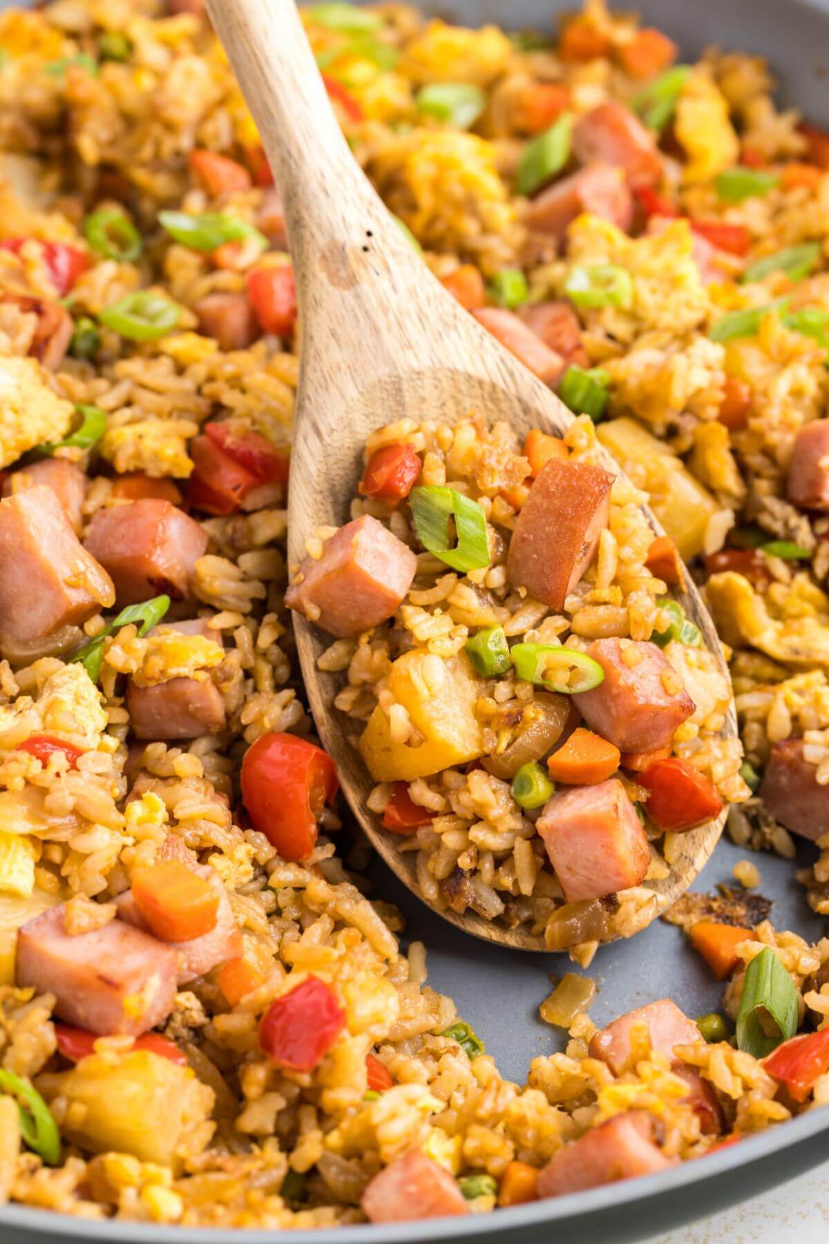 A wooden spoon scoops up fried rice from the pan.