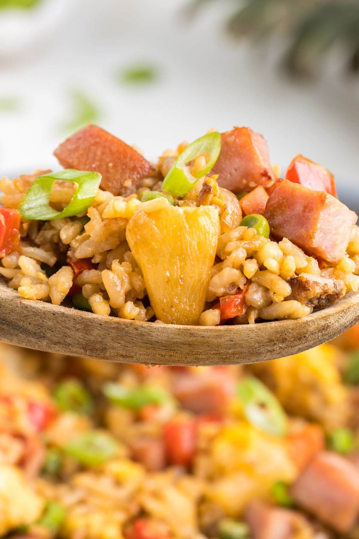 A wooden spoon holds fried rice in the air above a pan.